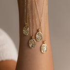 The Pearl Flower Birthstone Necklace, featuring a unique floral design in an oval frame with pearl accents, hangs from a raised arm against a neutral background.