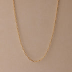 The Paperclip Chain Necklace is a delicate gold chain, ideal for layering and perfect for any style, shown on a beige background.
