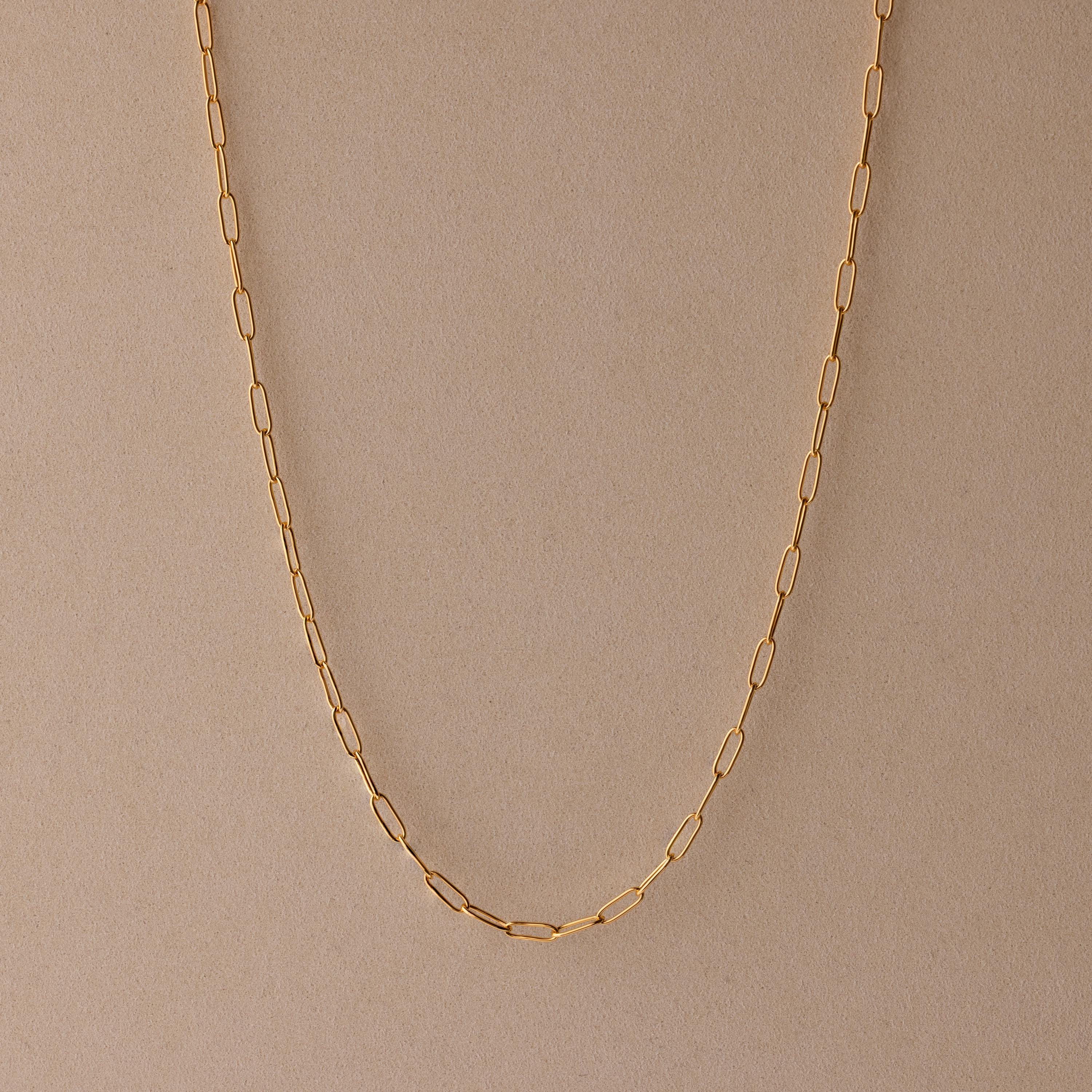 The Paperclip Chain Necklace is a delicate gold chain, ideal for layering and perfect for any style, shown on a beige background.