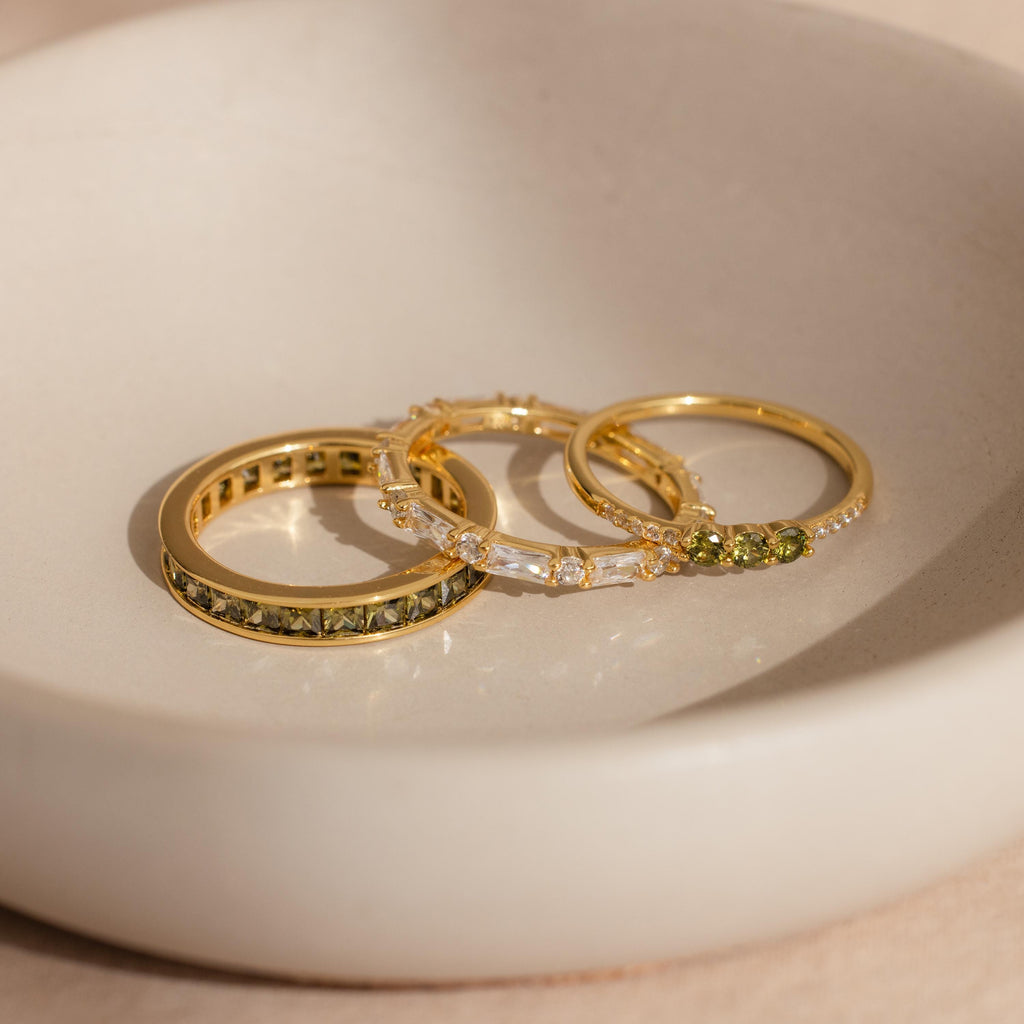 Trio of gold rings with peridot and diamond stones displayed in a ceramic dish.
