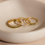 Trio of gold rings with peridot and diamond stones displayed in a ceramic dish.