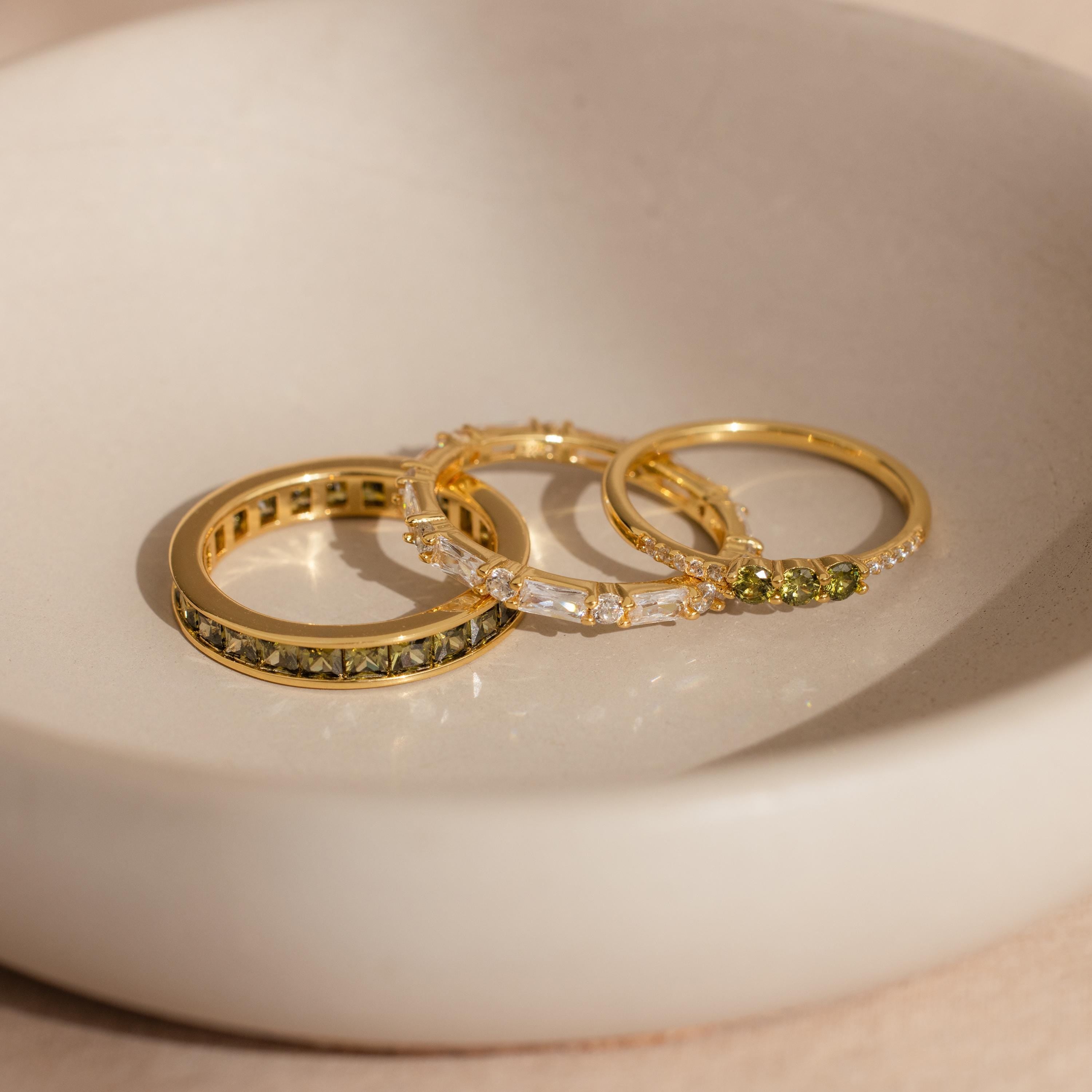 Trio of gold rings with peridot and diamond stones displayed in a ceramic dish.