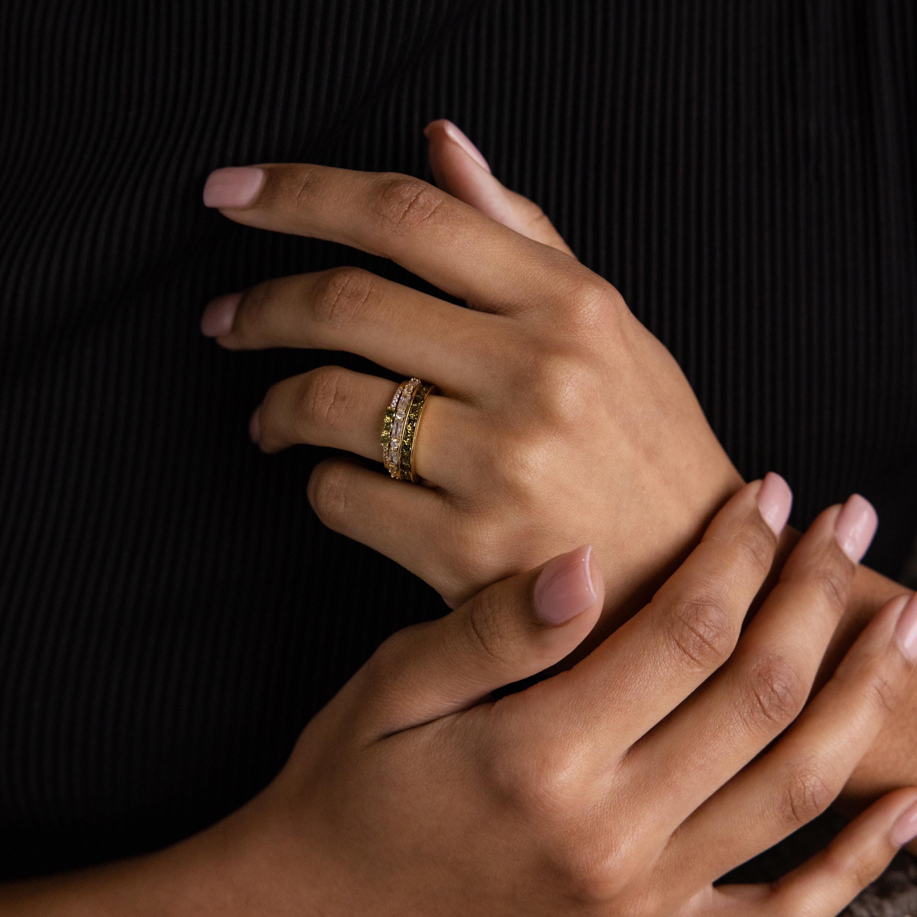 Model wearing a stacked set of peridot and diamond rings on one hand, styled with a black outfit.