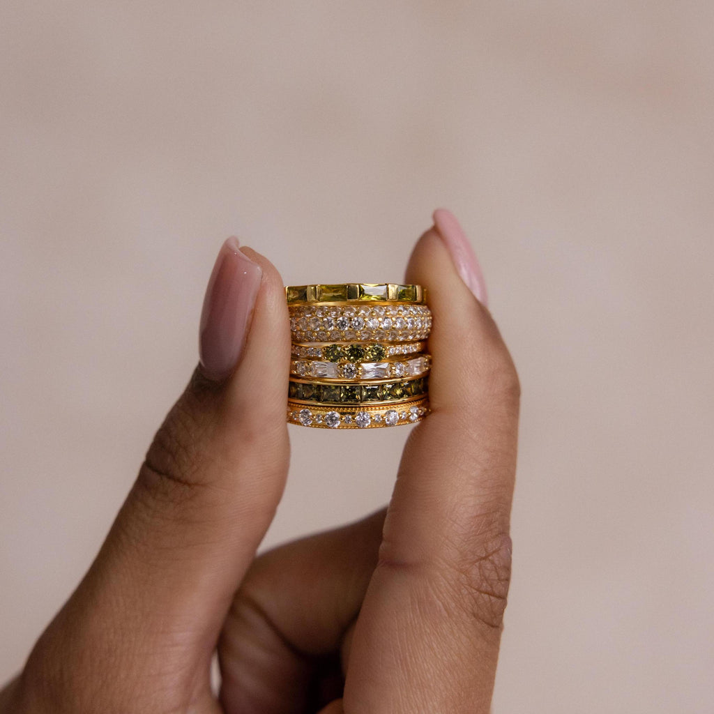 Hand holding a stack of gold peridot and diamond rings, showing the detailed stone settings.