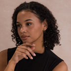 Woman with curly hair wearing Agate Diamond Chain Earrings and a black top, looking thoughtful with her hand near her chin.