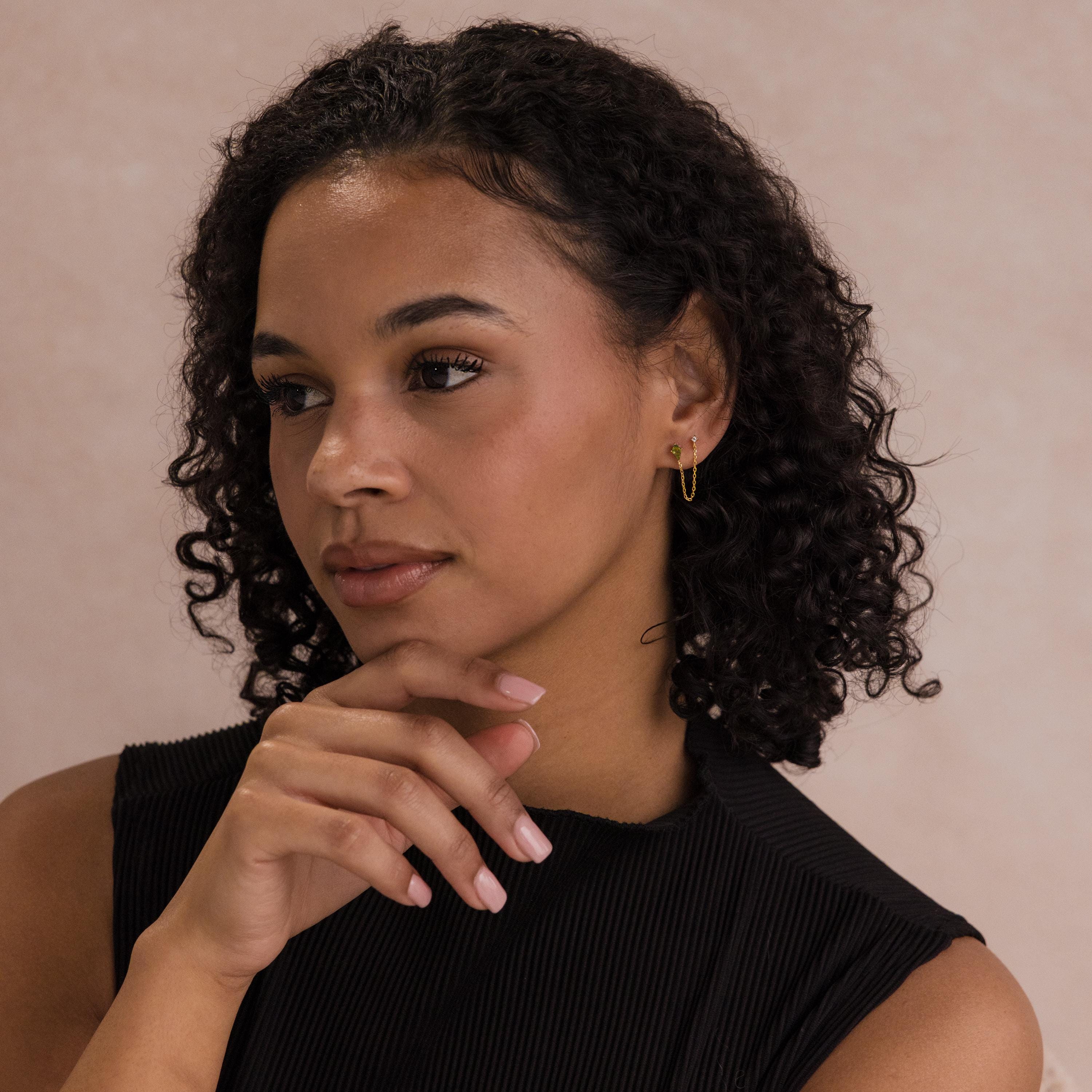 Woman with curly hair wearing Agate Diamond Chain Earrings and a black top, looking thoughtful with her hand near her chin.