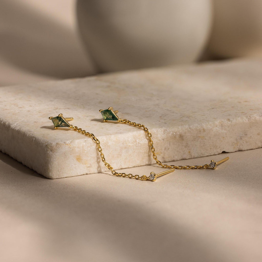 Agate Diamond Chain Earrings adorned with green moss agate stones and diamond accents, elegantly showcased on a beige marble surface.