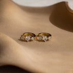 Princess Cut Birthstone Huggies are shown on a beige, wavy surface under soft lighting.