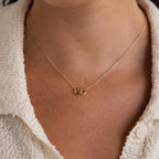 Wearing the Pave Interlocking Circle Necklace, featuring two linked gold rings symbolizing love, over a cream textured shirt.