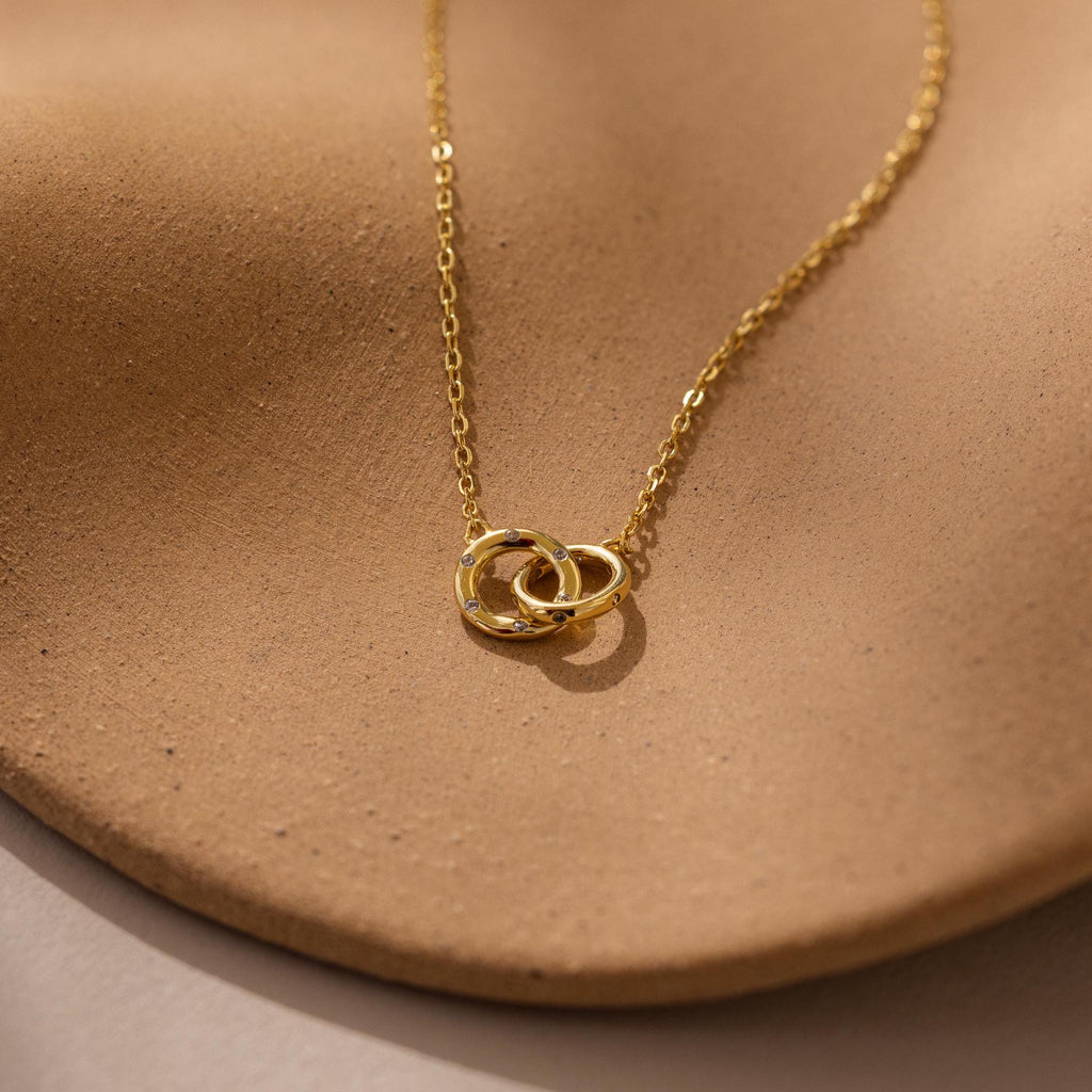 Pave Interlocking Circle Necklace featuring two rings, symbolizing love, shown on a textured light brown surface.