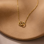 Pave Interlocking Circle Necklace featuring two rings, symbolizing love, shown on a textured light brown surface.