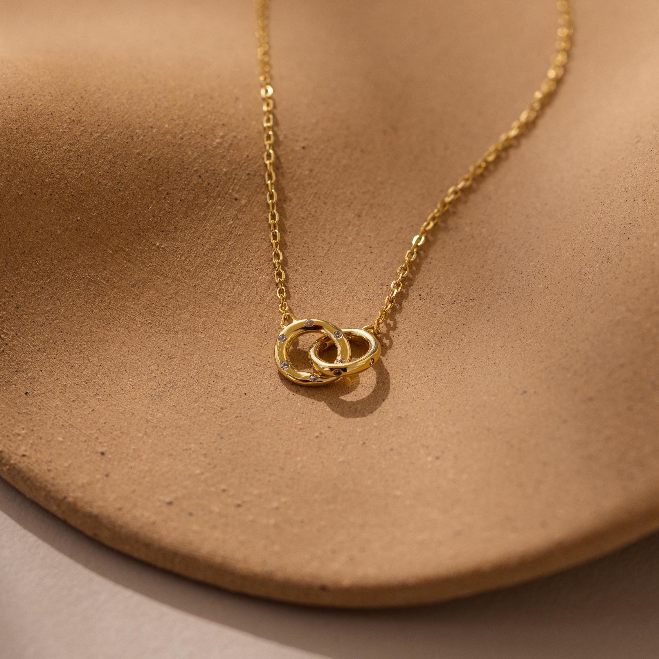 Pave Interlocking Circle Necklace featuring two rings, symbolizing love, shown on a textured light brown surface.