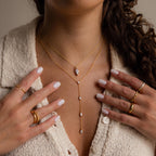 A woman wearing the Mixed Diamond Lariat Necklace, layered with gold and diamond details, paired with rings and a cream textured button-up top and white nails.