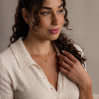 Woman with curly hair wearing a cream textured blouse and the Dainty Bubble Letter Necklace in 18K Gold, looking slightly to the side.