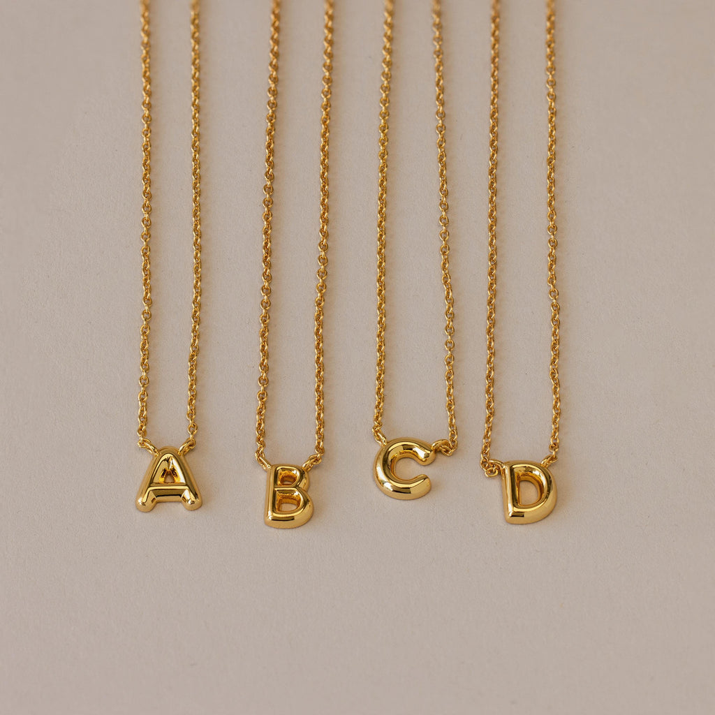 Four Dainty Bubble Letter Necklaces in 18K Gold, featuring A, B, C, and D pendants, displayed on a neutral background—ideal for a minimalist personalized accessory.