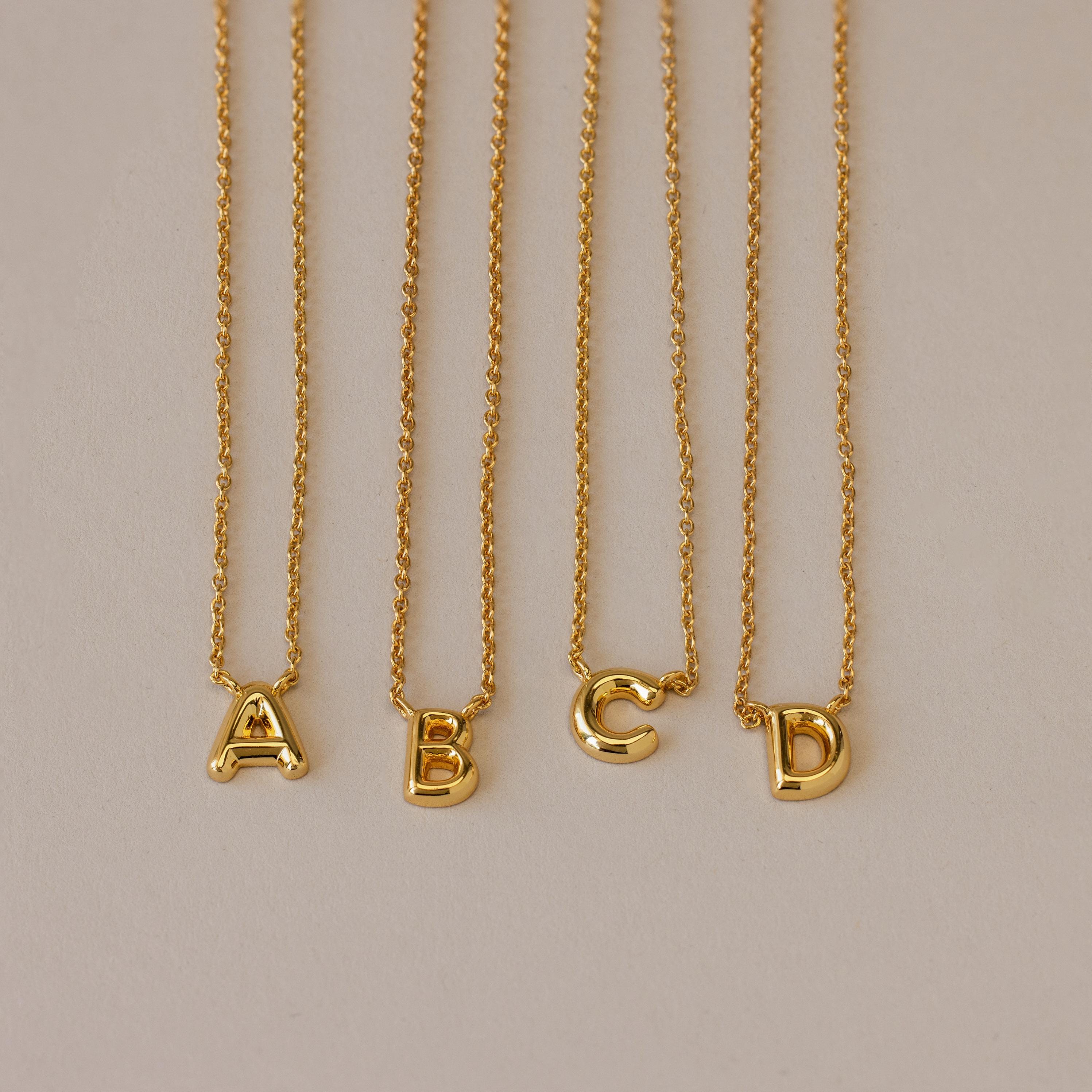 Four Dainty Bubble Letter Necklaces in 18K Gold, featuring A, B, C, and D pendants, displayed on a neutral background—ideal for a minimalist personalized accessory.