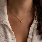 A person in a white textured shirt wears the Dainty Bubble Letter Necklace, featuring a minimalist bubble letter A pendant.