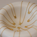 Dainty Bubble Letter Necklaces with gold letter pendants are arranged in a white bowl, displaying a variety of alphabet letters for a chic personalized necklace showcase.