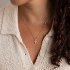 A woman wears the Diamond Cross Necklace—a gold faith necklace with pavé CZ diamonds and a small cross pendant—paired with a cream knit top; focus is on her neck and collar.