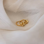 Dangling Blossom Huggies—two gold huggie hoops with delicate flower designs—rest atop soft, light beige fabric, capturing their unique charm.