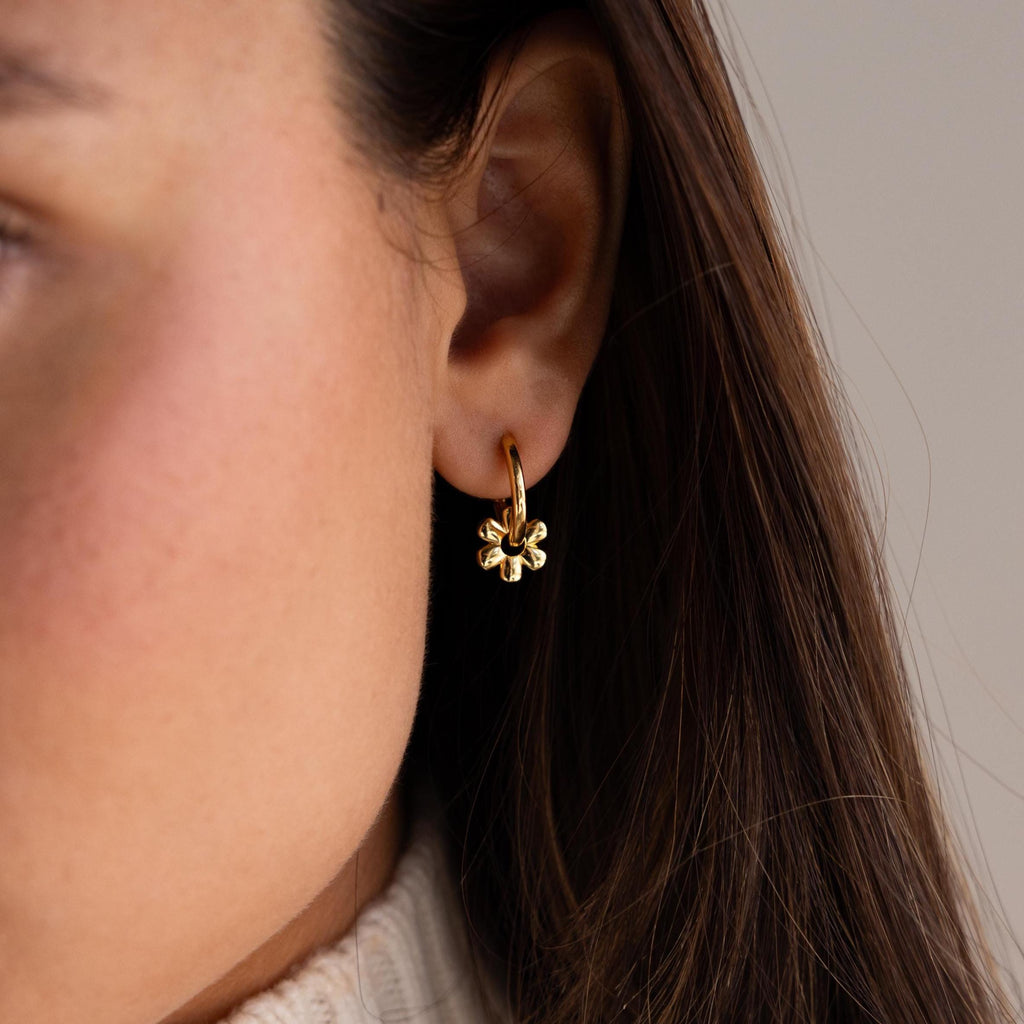 Close-up of a woman's ear wearing Dangling Blossom Huggies—petite hoops with delicate flower-shaped charms, perfect for fans of floral earrings.