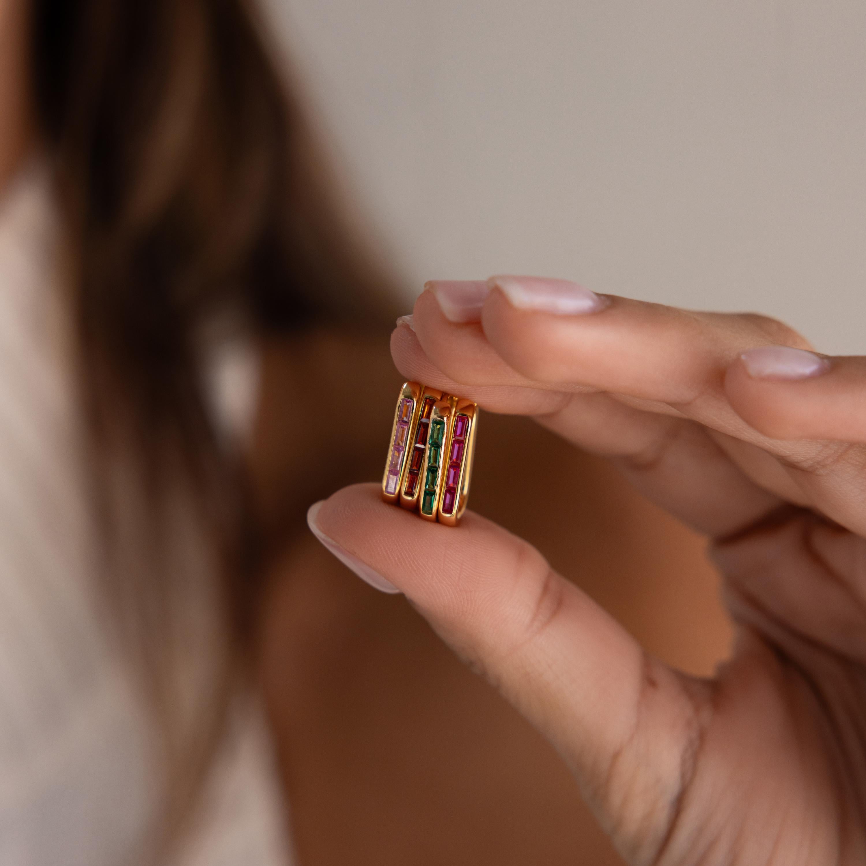 A hand holds a small, colorful, rectangular object with gold edges and gemstone-like details, reminiscent of the customizable gemstones featured in Baguette Birthstone Link Earrings.