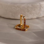 Baguette Birthstone Link Earrings: gold geometric hoops with rectangular red stones, displayed on a smooth beige surface beside a textured white stone.
