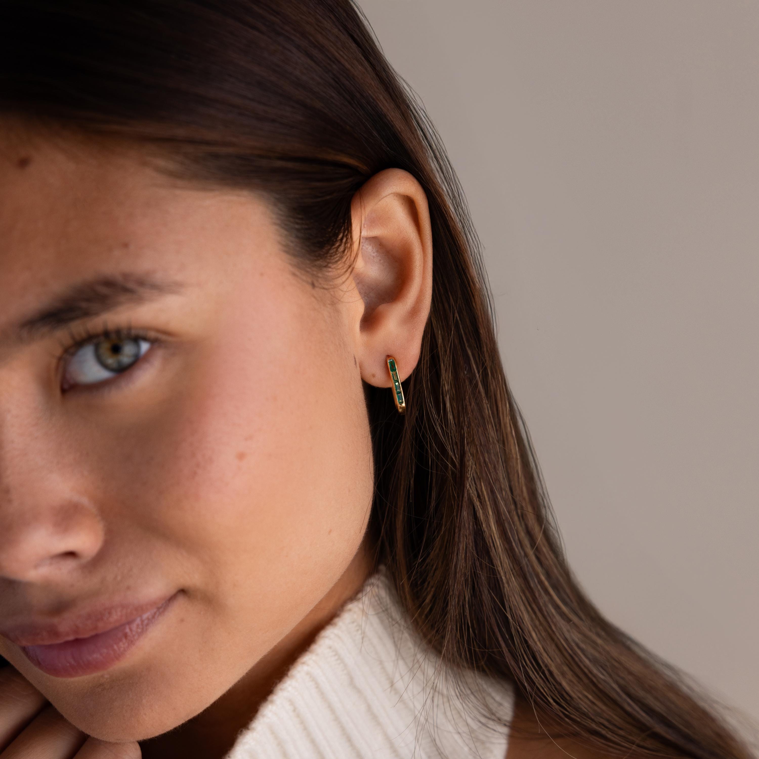 A woman with long brown hair wears Baguette Birthstone Link Earrings and a cream turtleneck sweater, adding a modern twist to her understated style.