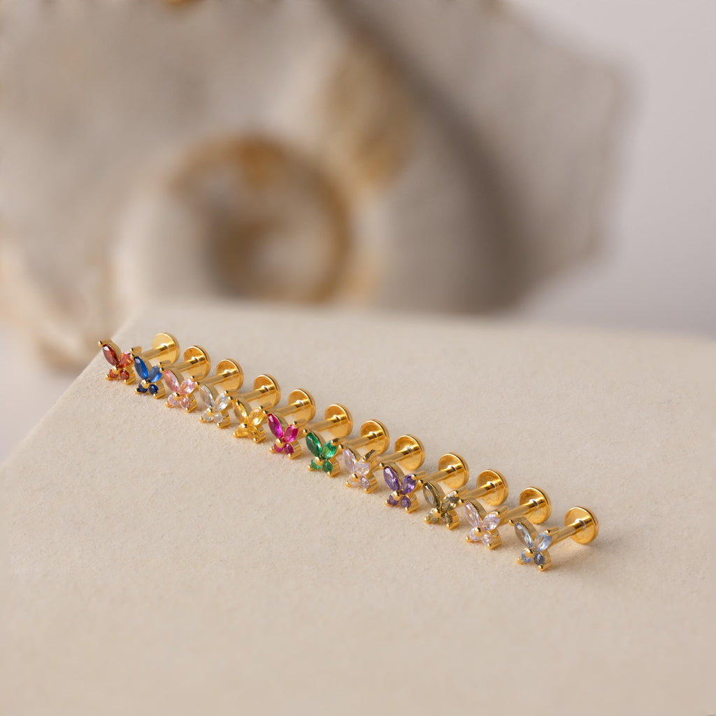 A row of Butterfly Birthstone Flatback Studs featuring colorful gemstones, ideal for personalized jewelry, displayed on a beige surface.