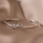 The Duo Knot Bangle features a rope texture and is showcased on a soft beige fabric, making it an elegant gift for any occasion.