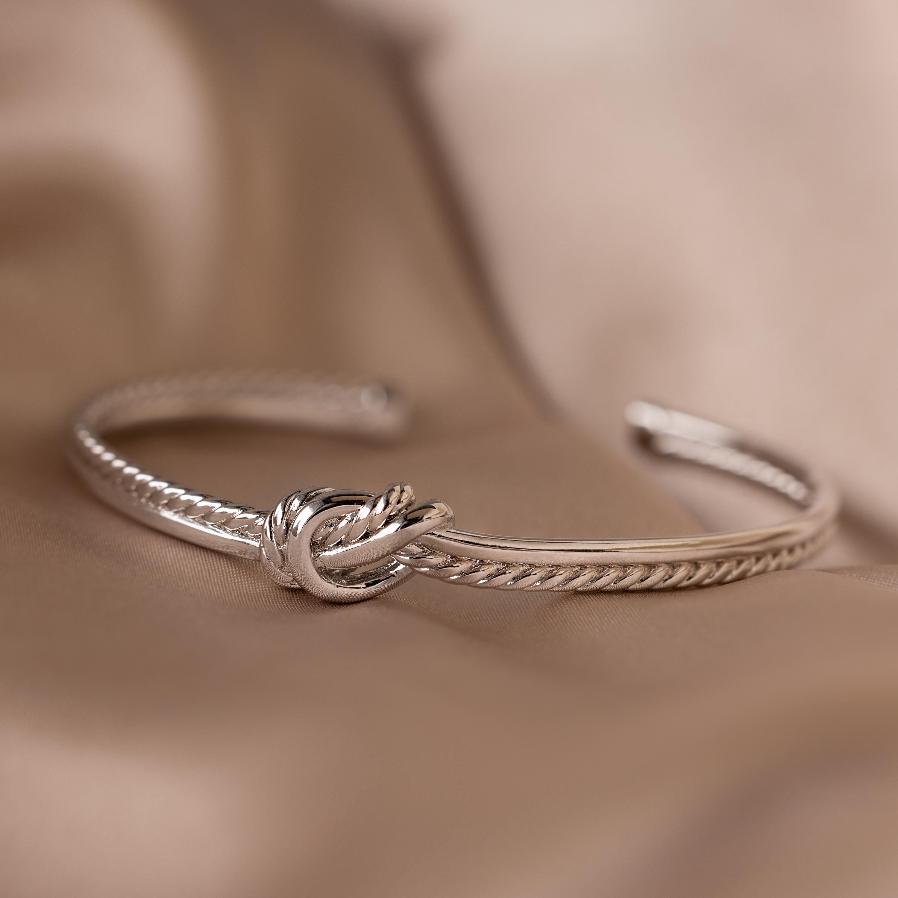 The Duo Knot Bangle features a rope texture and is showcased on a soft beige fabric, making it an elegant gift for any occasion.