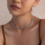 A woman wearing the Strap Necklace, a chunky silver chain with interwoven links, paired with a brown spaghetti strap top, shown from shoulders up.