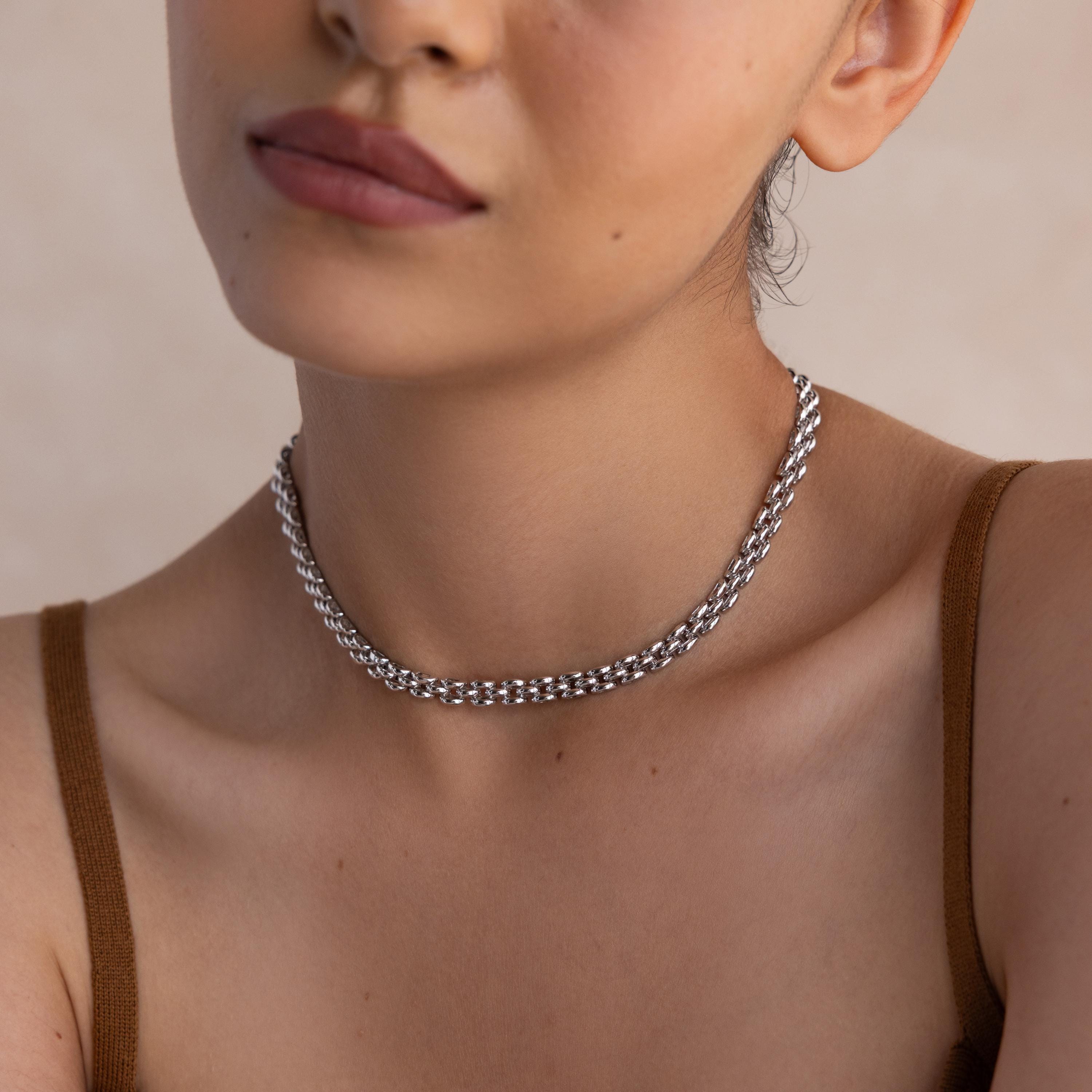 A woman wearing the Strap Necklace, a chunky silver chain with interwoven links, paired with a brown spaghetti strap top, shown from shoulders up.