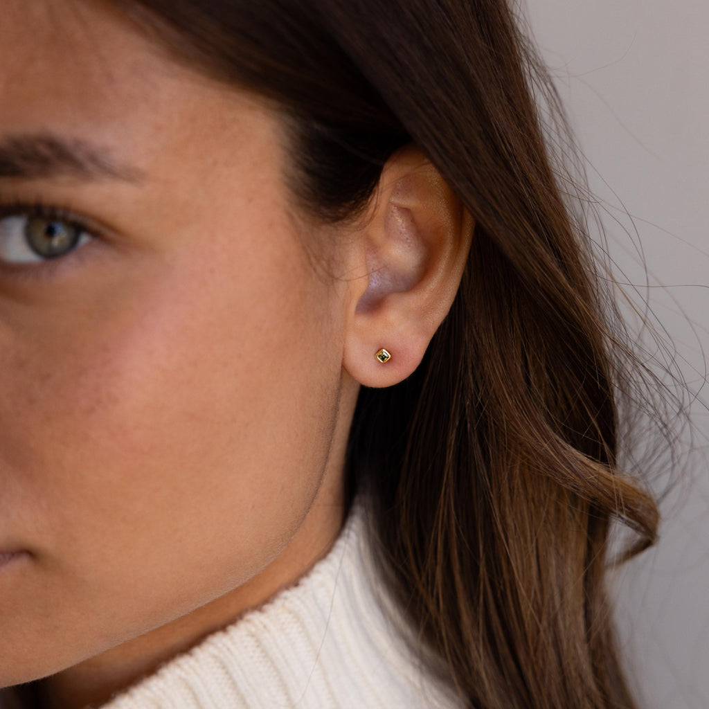 Close-up of a woman wearing Square Bezel Blue Zircon Flatback Studs and a cream turtleneck sweater.