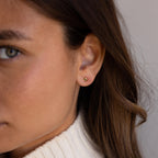 Close-up of a woman wearing Square Bezel Blue Zircon Flatback Studs and a cream turtleneck sweater.
