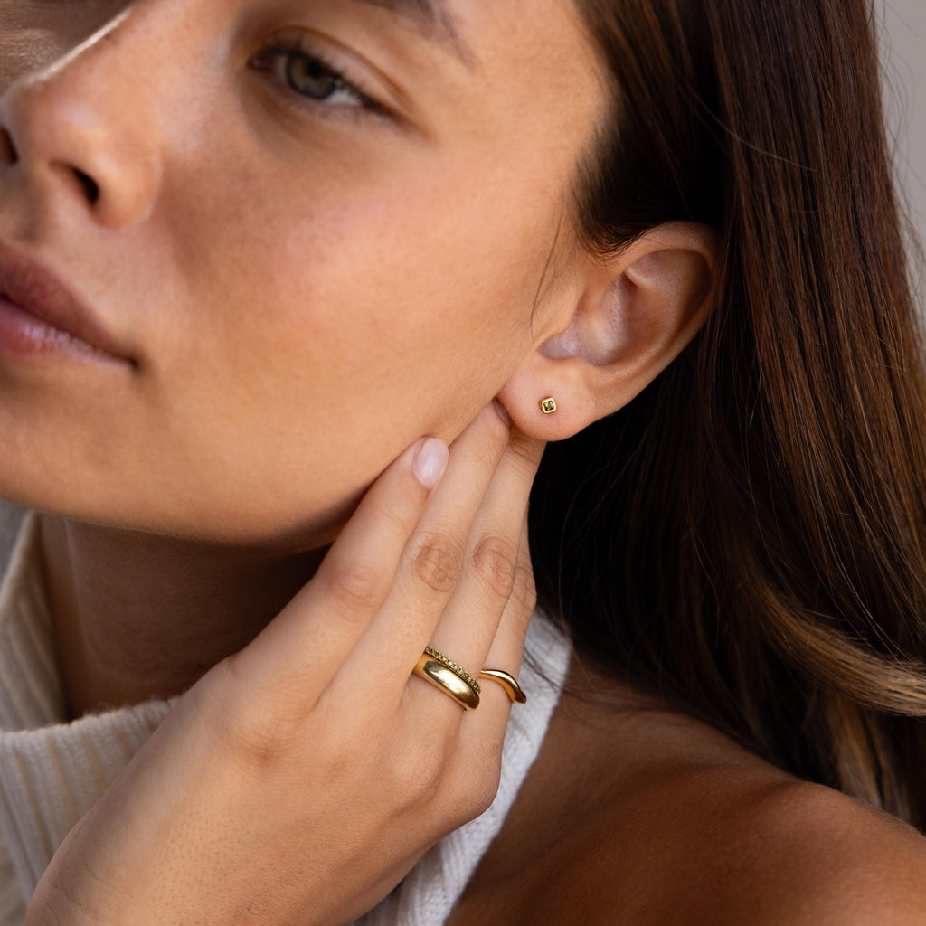 Close-up of a woman wearing Square Bezel Pink Tourmaline Flatback Studs and rings, gently touching her ear and face.