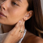Close-up of a woman wearing Square Bezel Pink Tourmaline Flatback Studs and rings, gently touching her ear and face.