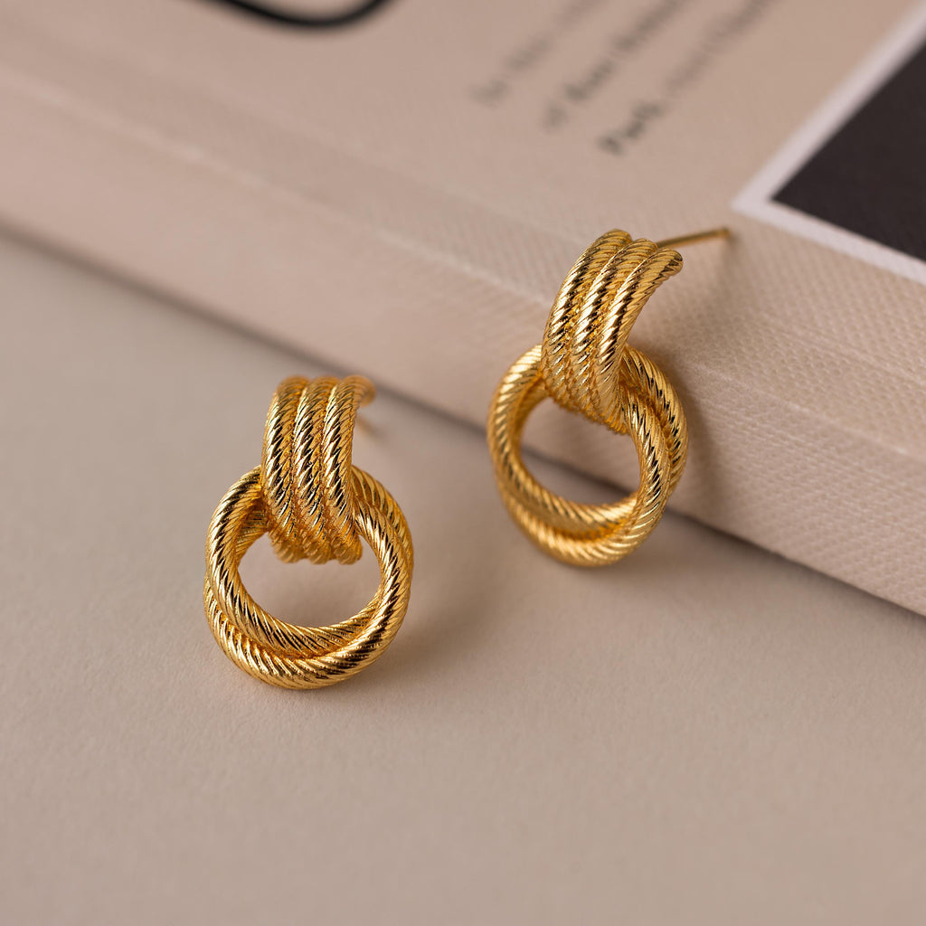 The Ribbed Duo Knot Earrings, featuring a gold twisted rope design, are stylish modern statement earrings—ideal for any look and perfect for elevating your style.