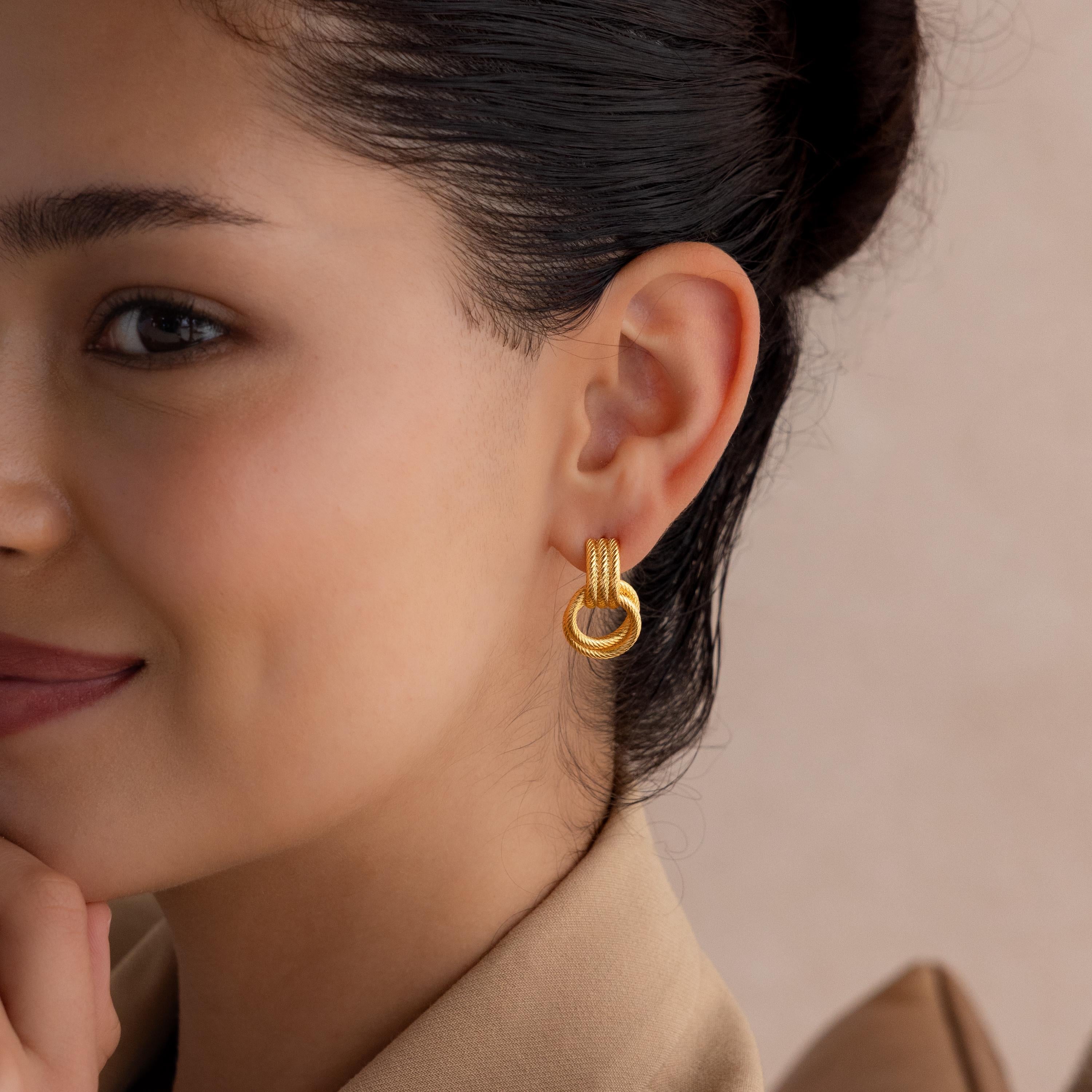 Woman with dark hair wearing Ribbed Duo Knot Earrings and a beige blazer, smiling slightly.