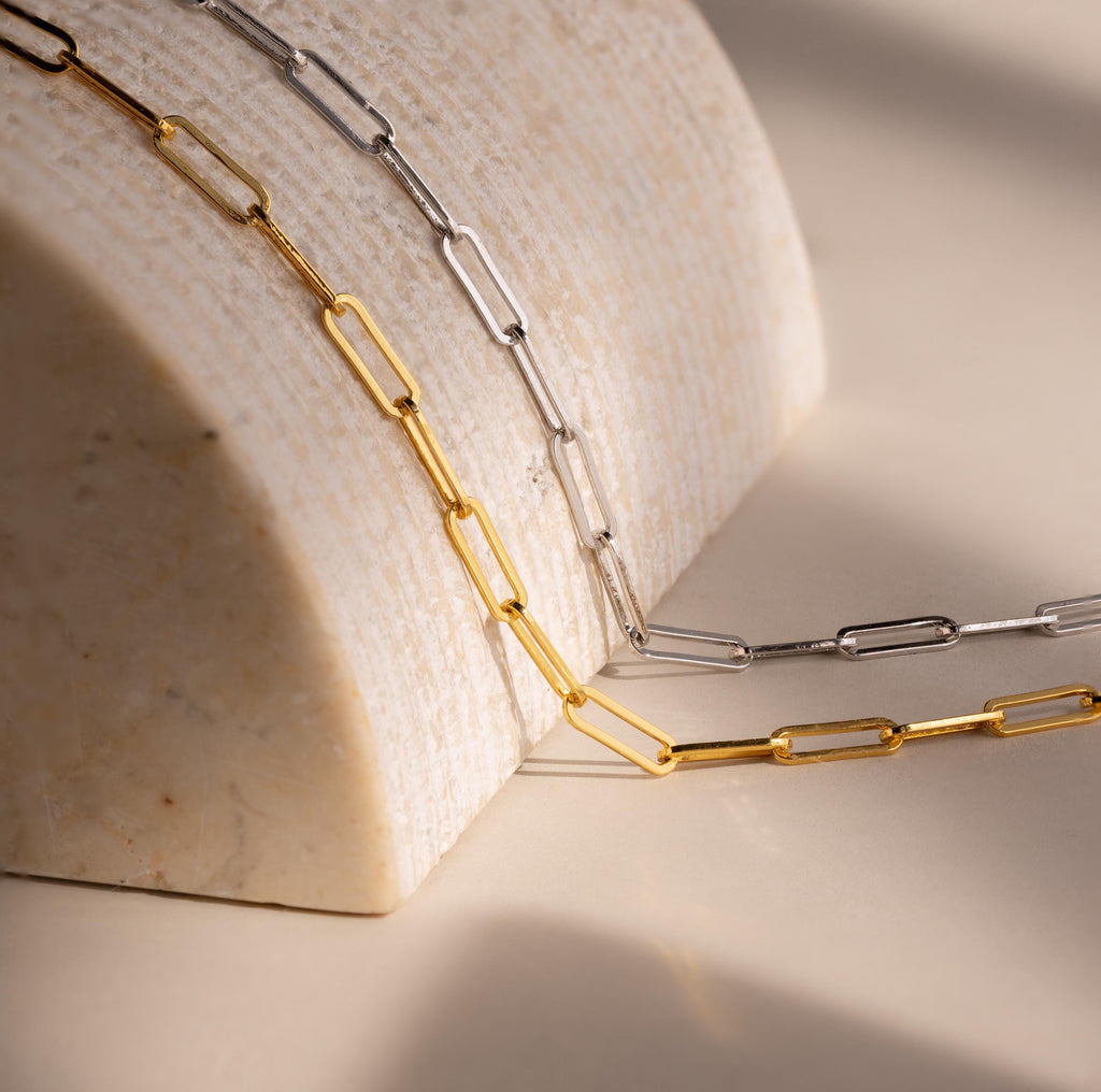 The Bold Paperclip Chain Necklace drapes elegantly over a curved marble surface in soft lighting, making a striking statement for a bold necklace look.