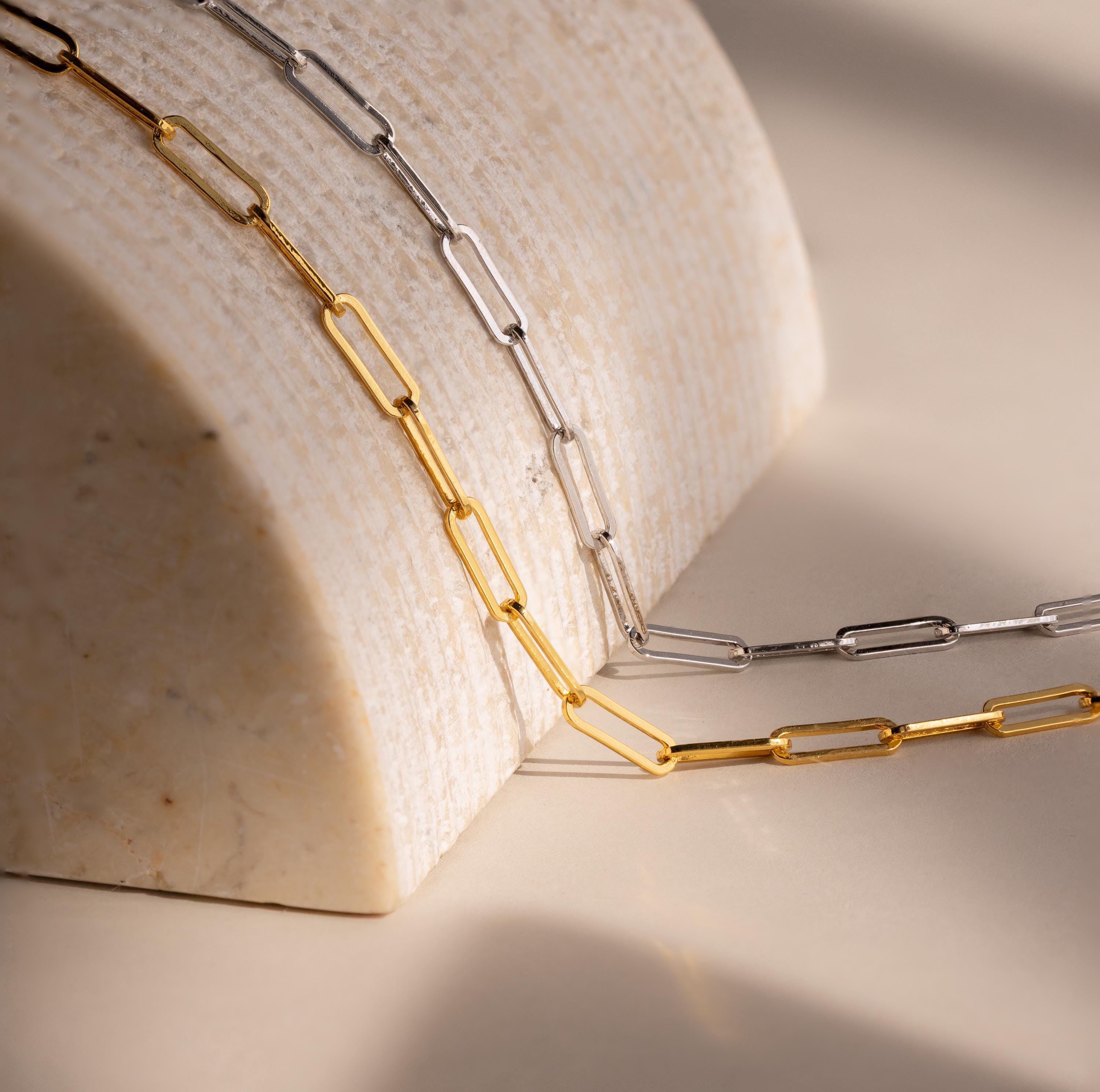 The Bold Paperclip Chain Necklace drapes elegantly over a curved marble surface in soft lighting, making a striking statement for a bold necklace look.