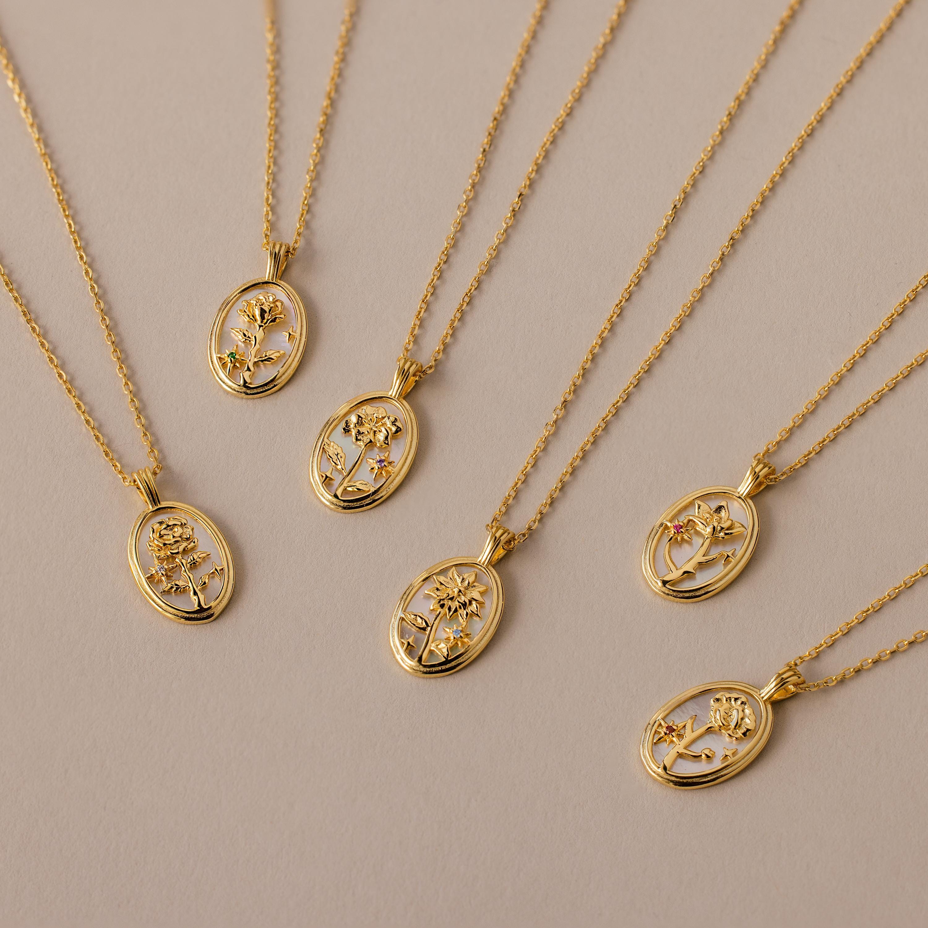 The Pearl Flower Birthstone Necklace, a gold piece with an oval mother of pearl pendant and delicate floral design, shines elegantly on a neutral beige background, showcasing refined beauty.