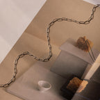 A minimalist piece, the Paperclip Chain Necklace is shown on an open magazine featuring a simple beige-toned interior.