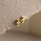 Princess Cut Birthstone Huggies featuring opal-like stones displayed on a textured beige paper background.