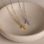 Two Diamond Cross Necklaces, one gold and one silver with pave CZ diamonds, are displayed in a simple beige dish.