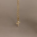 Gold chain with a small, pave CZ diamond cross pendant against a plain beige background, offering a playful twist on classic faith necklace designs.