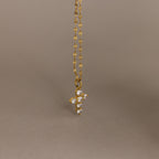 Gold chain with a small, pave CZ diamond cross pendant against a plain beige background, offering a playful twist on classic faith necklace designs.