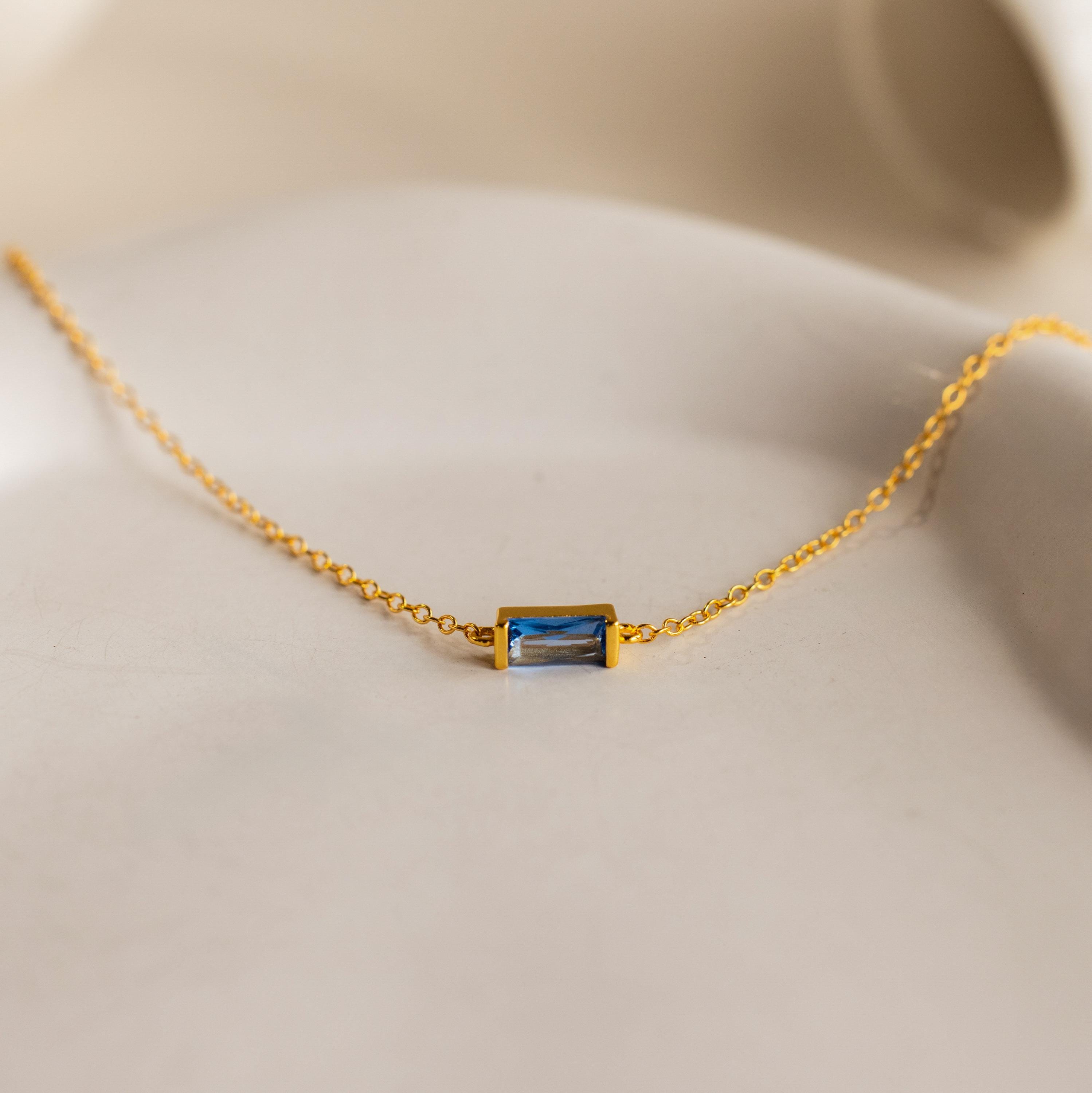 Gold chain necklace with a small rectangular blue gemstone pendant on a soft beige background, perfect for pairing with the Dainty Baguette Birthstone Bracelet for an elegant, coordinated look.