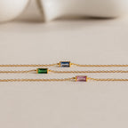 Three gold chain necklaces with rectangular blue, green, and purple gemstones are displayed on a neutral background, reflecting the refined elegance of the Dainty Baguette Birthstone Bracelet.