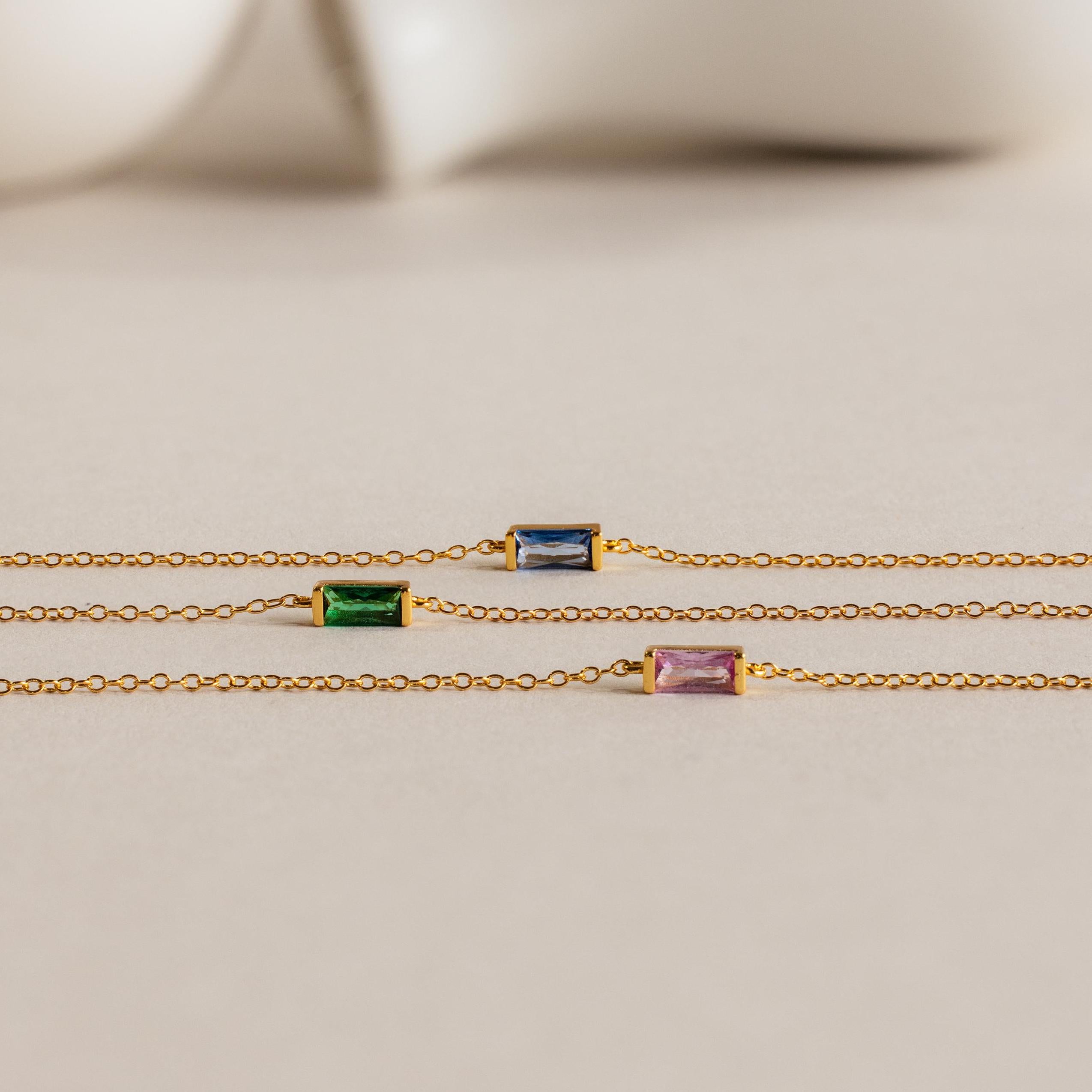Three gold chain necklaces with rectangular blue, green, and purple gemstones are displayed on a neutral background, reflecting the refined elegance of the Dainty Baguette Birthstone Bracelet.